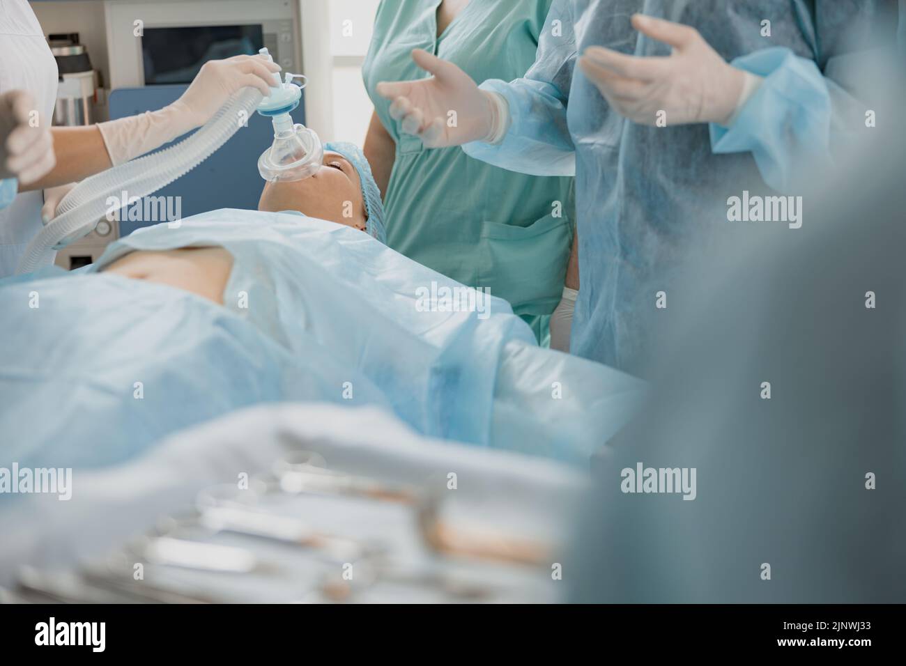 Close up hands of doctor anesthesiologist holding breathing mask on patient face during operation Stock Photo