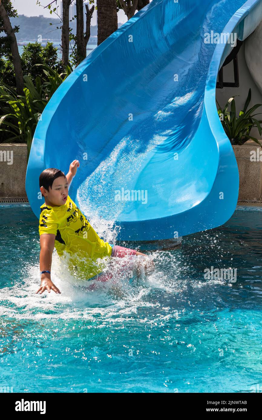 Young boy playing on water slide at swimming pool at beachfront hotel, Pattaya, Chon Buri, Thailand Stock Photo