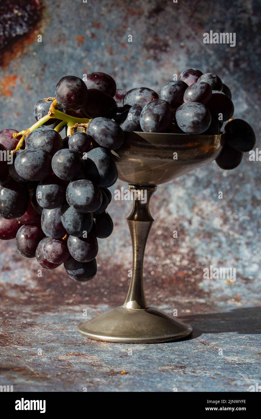 Bunch of black grapes in an old pewter goblet. On a grunge background