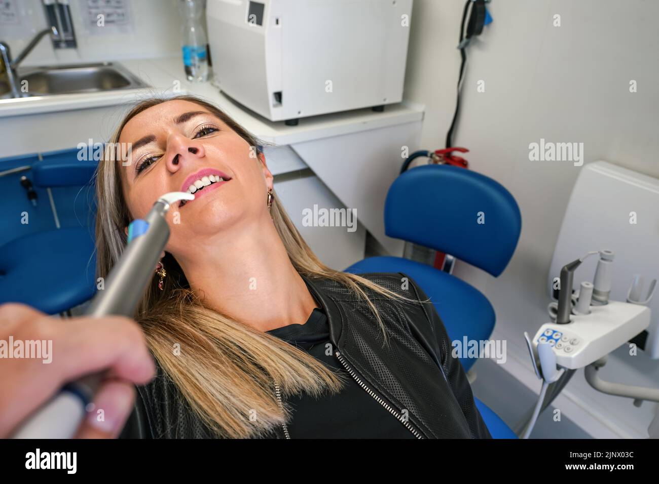 Young woman posing with her mouth half open at dentist chair, dental tool near her teeth, first person view Stock Photo