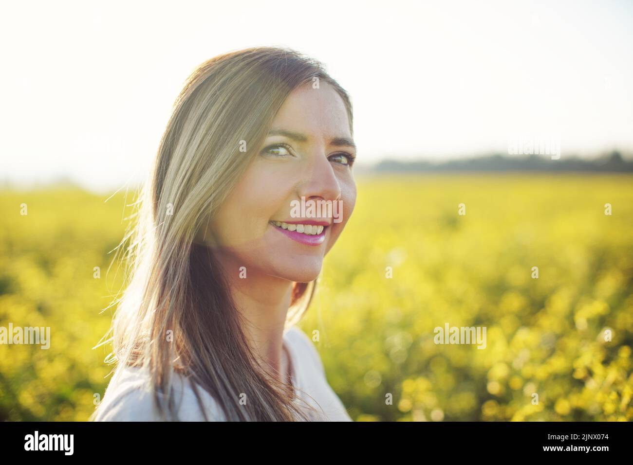 Portrait of young woman with long hair, yellow flower field and sun backlight behind her Stock Photo