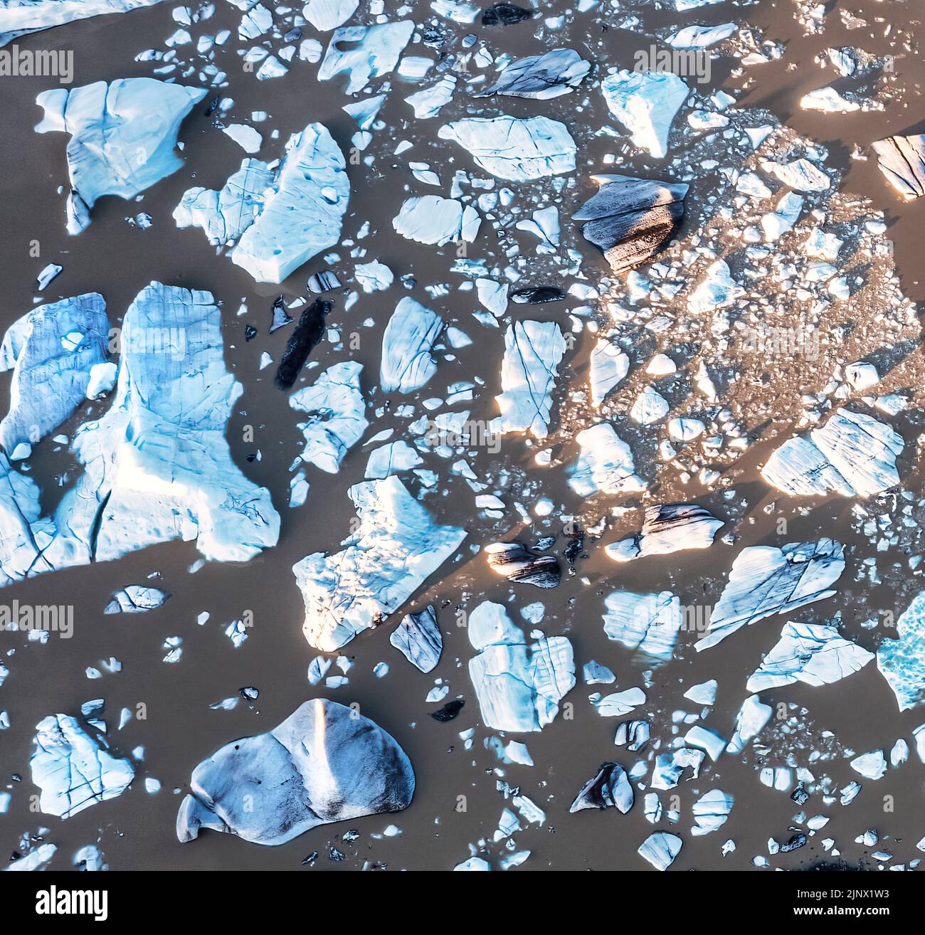 Overhead view of blue icebergs in the Fjallsarlon glacier lagoon, southern Iceland. The surrounding water is brown due to volcanic silt deposits. Dron Stock Photo
