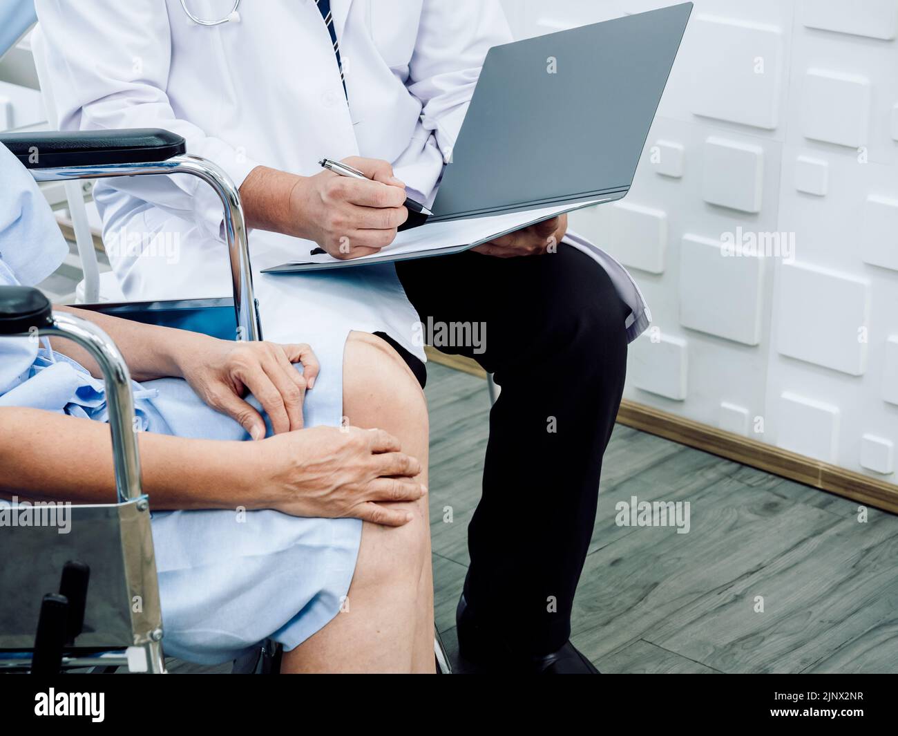 Doctor's hand using pen writing on patient medical record file. The surgeon is explaining the results of knee surgery on a senior or elderly old lady Stock Photo