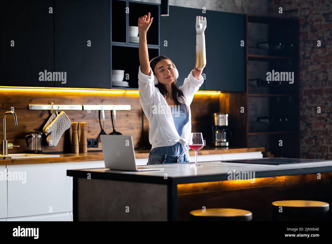 Happy girl with prosthetic arm listening music headphones kitchen at home, woman with disability relaxing and dancing. Stock Photo