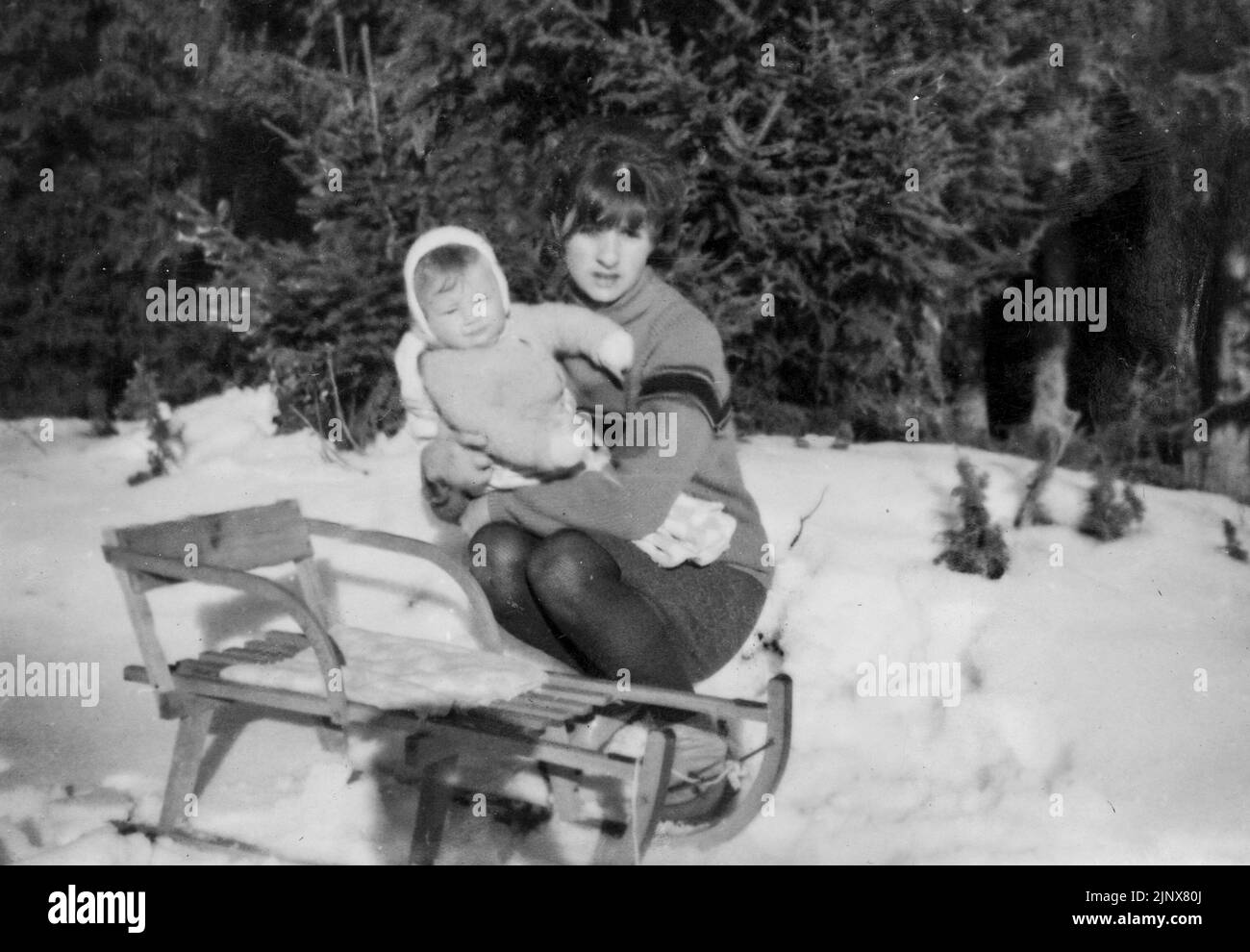Mother holding her baby by simple wooden sleigh in snow 1970 rural Bulgaria Stock Photo