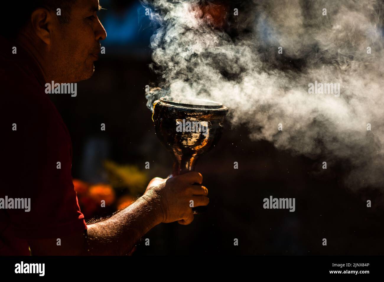 A Mexican man, holding a smoking incense burner, performs a purification of a tomb during the Day of Dead celebrations in Tlapa de Comonfort, Mexico. Stock Photo