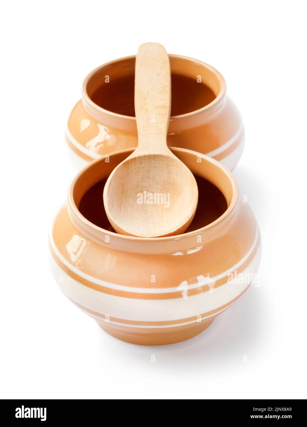 Glazed ceramic pots for cooking with wooden spoon on a white background ...