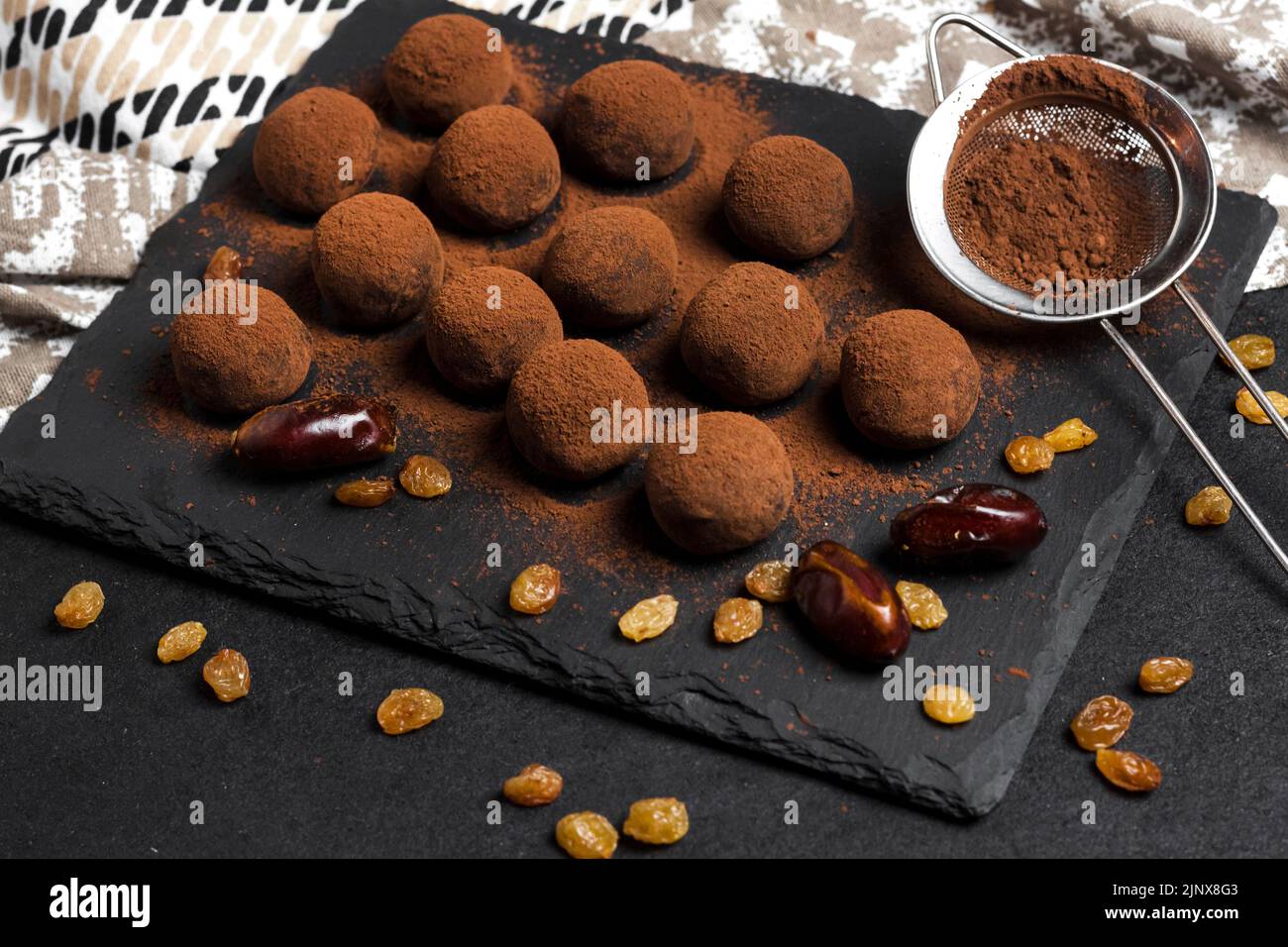 Homemade vegan truffles with dried fruits, walnuts and raw cocoa powder served on black slate plate. Stock Photo