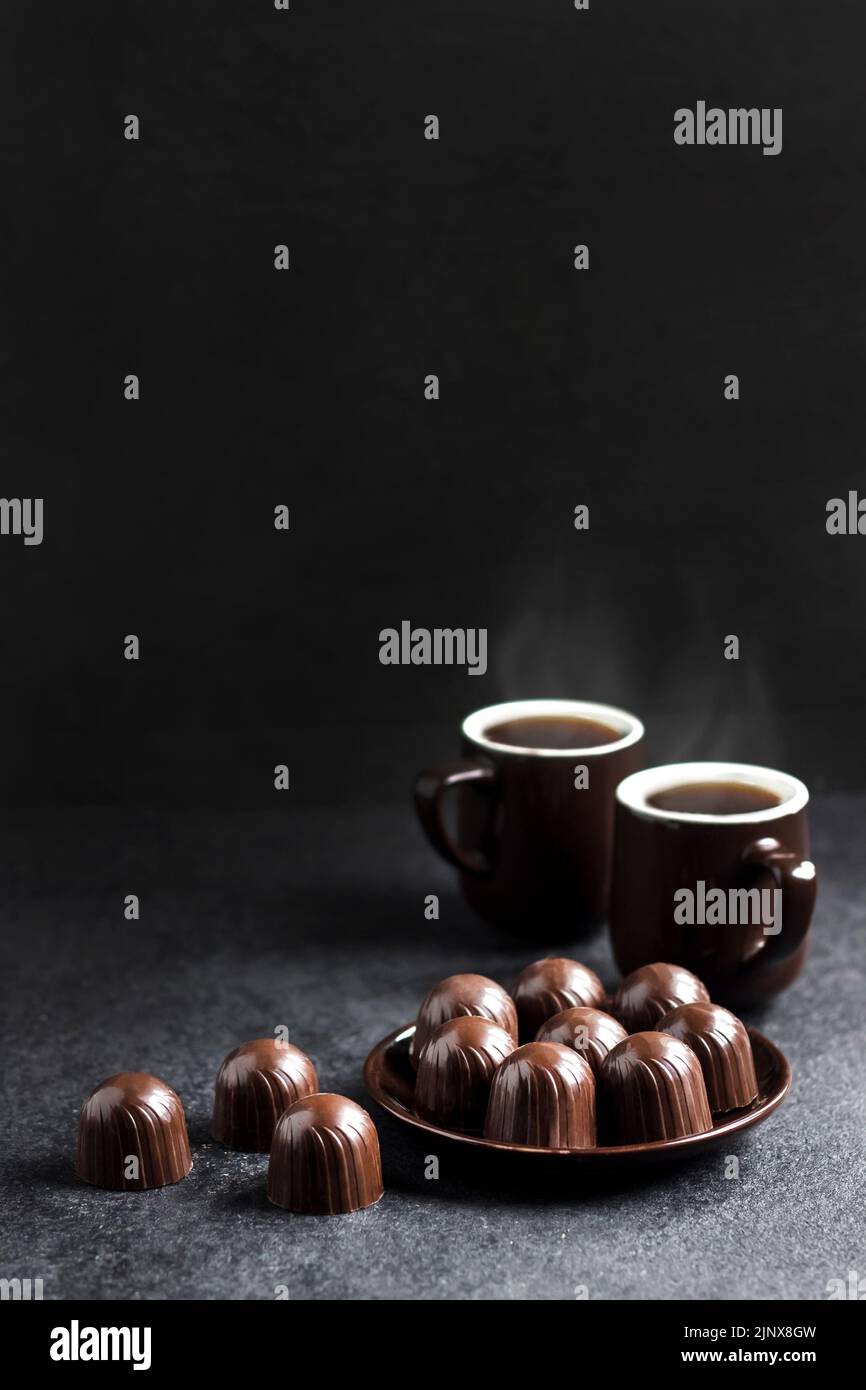 Chocolate candies on a plate and two cups of hot coffee on black background with copy space Stock Photo