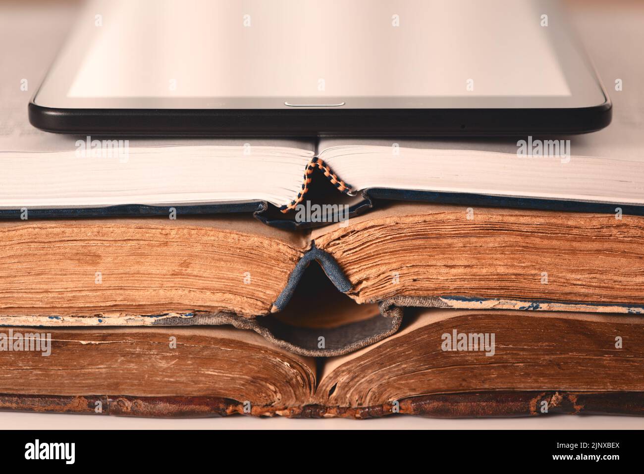 Open pages of old shabby brown and new books, digital tablet. Concept of choice between new technologies and old books. Analog vs digital. Closeup Stock Photo
