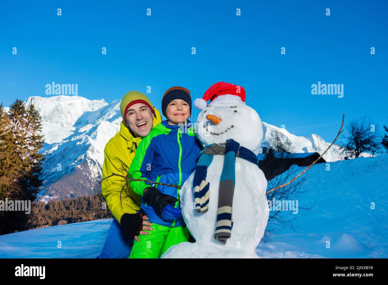 Boy and dad playing with newly made snowman in the mountains Stock Photo