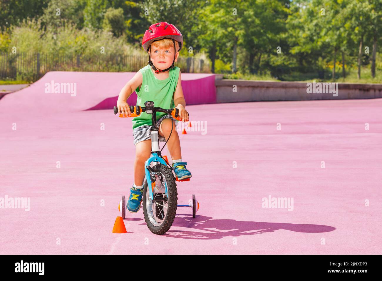 Blond boy ride small bicycle with learning wheels around cones Stock