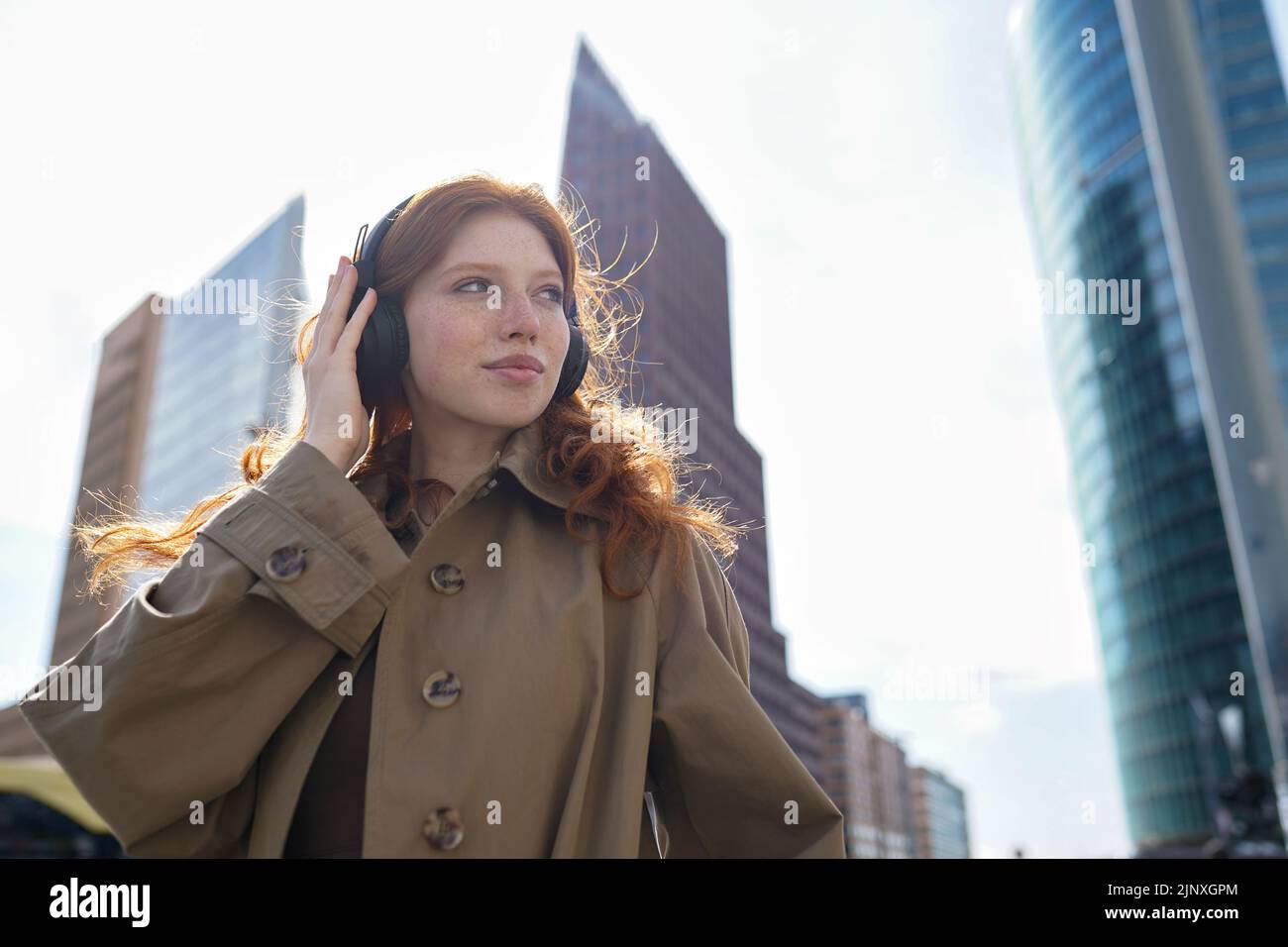 Teen redhead girl wearing headphones listening music in big city. Stock Photo
