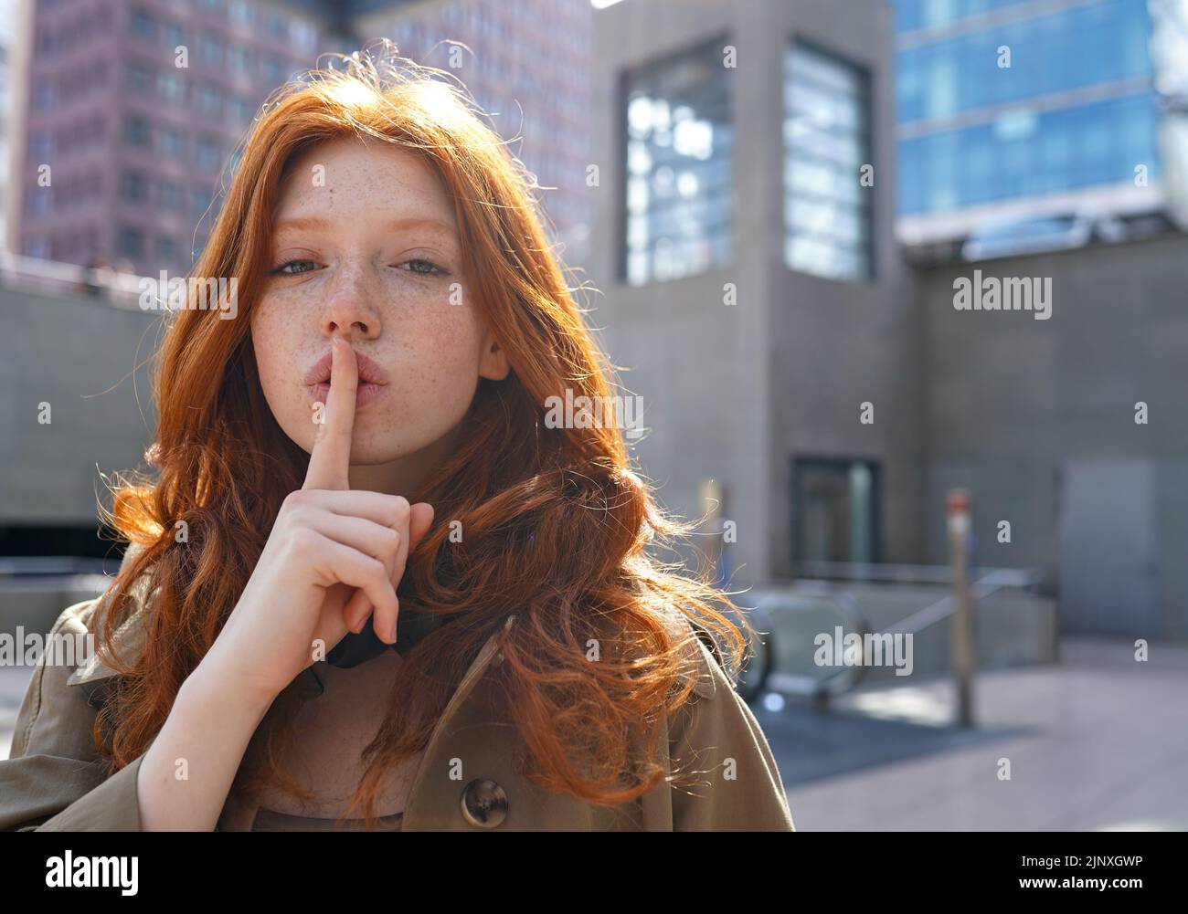 Hipster teen cool redhead fashion girl showing shh sign in city. Stock Photo