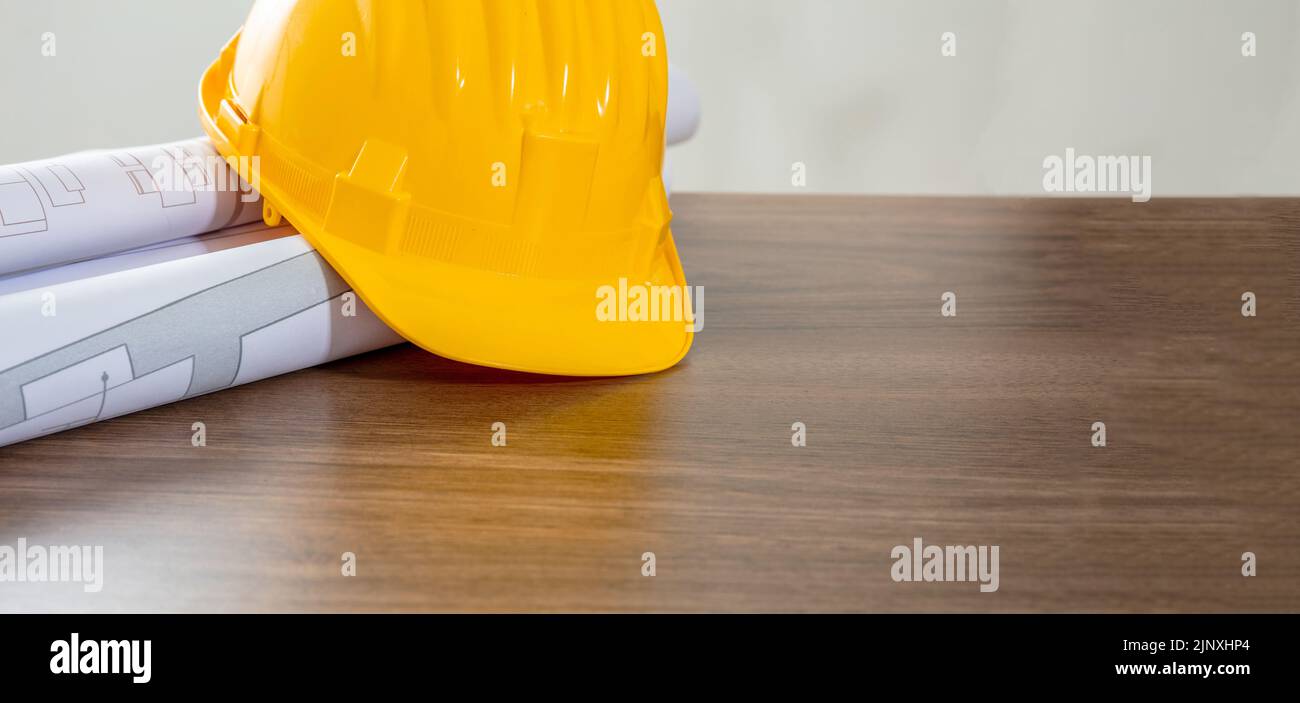 Construction project. Yellow safety helmet and building blueprint plans on wooden table, copy space. Architect engineer office Stock Photo