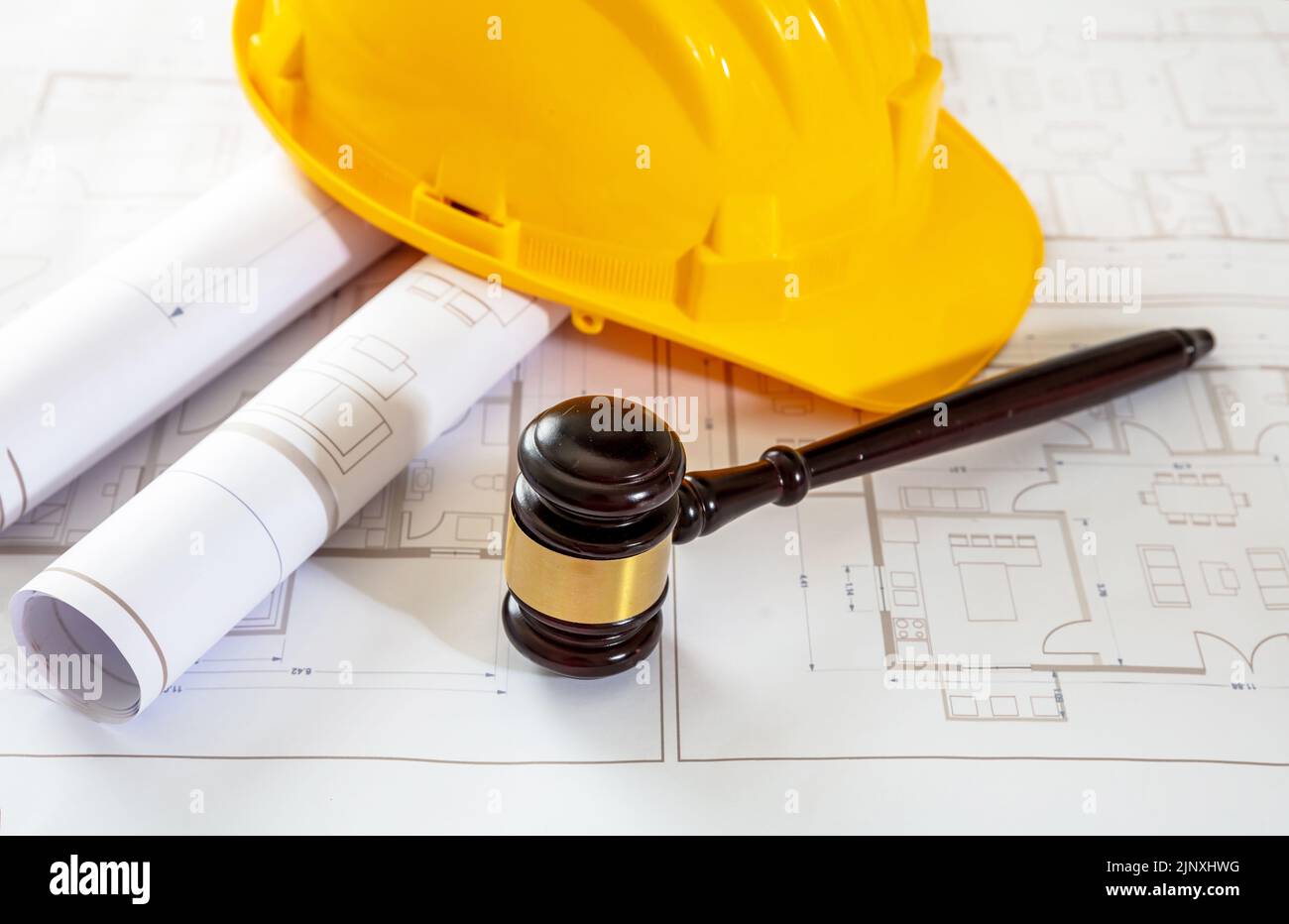 Labor, Construction law. Yellow safety hardhat and judge gavel on building blueprint plans Stock Photo
