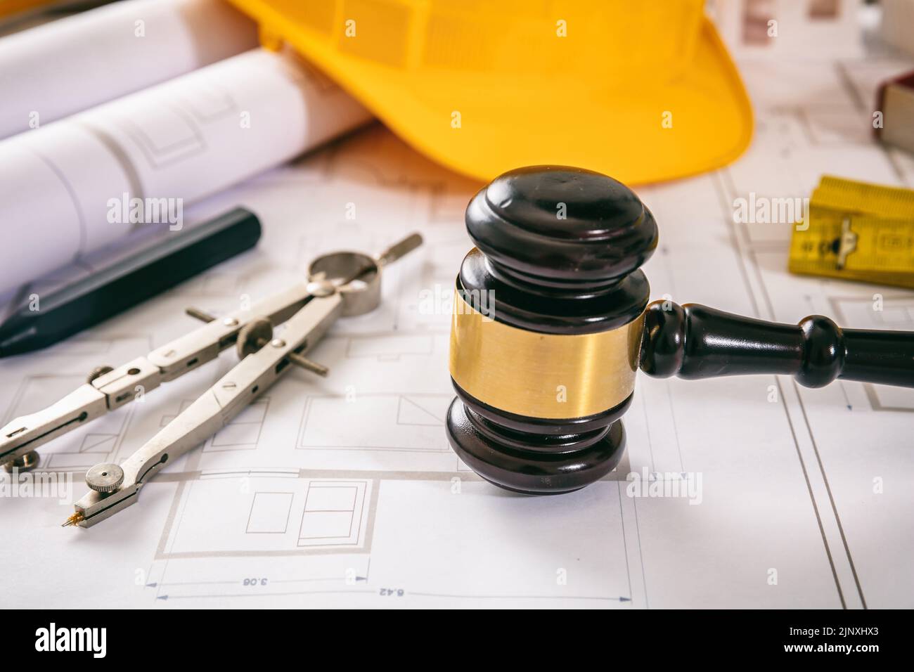 Construction and Labor law. Yellow safety helmet and judge gavel on building blueprint plans, close up view. Stock Photo