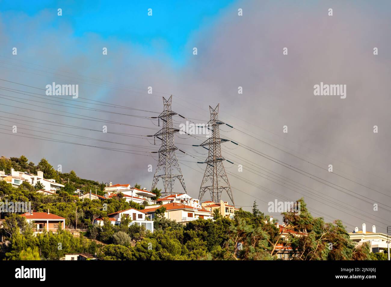 Greece on fire. Heavy dark grey smoke because of fire at Athens forest. Nature disaster, ash and smoke on gray sky over hill with trees and habitable Stock Photo