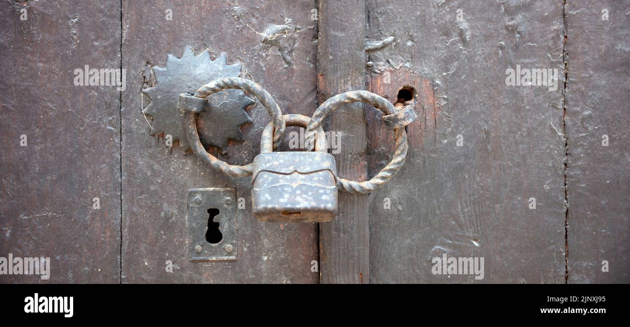 Old vintage wooden door locked with rusty padlock on metal double handle. Close up view of keyhole and safe closed entrance with padlock. No access co Stock Photo