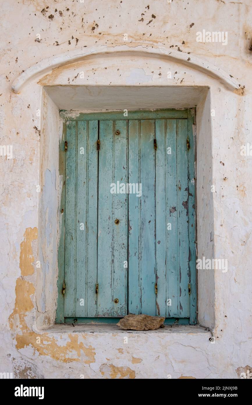 Aged wooden closed shutters with rusty hinges, peeled building wall facade. Abandoned house, stone keep the faded blue window planks shut. Vertical Stock Photo