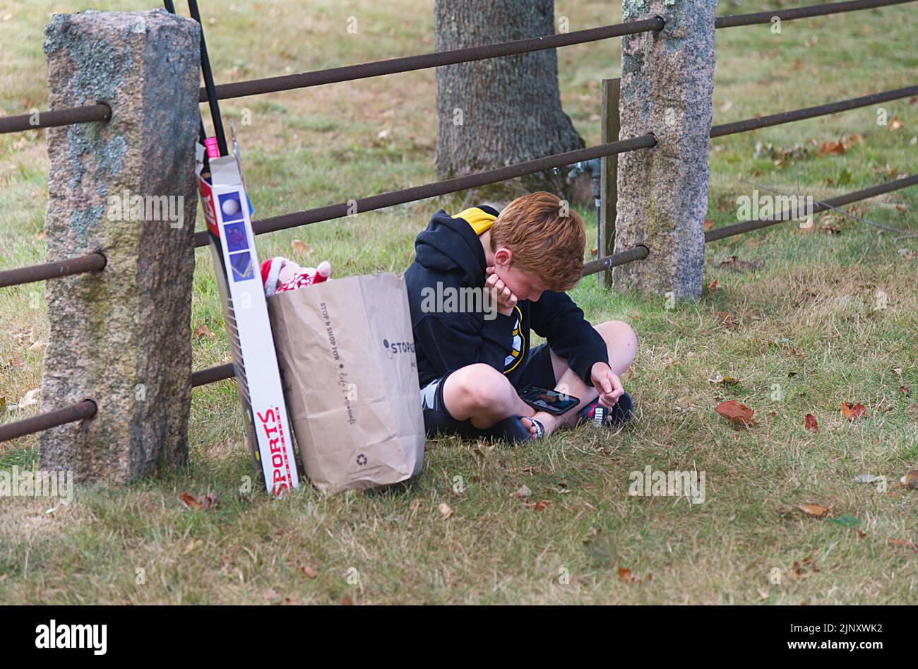 A young boy bored and checking his phone at a church flea market in Dennis, Massachusetts on Cape Cod Stock Photo