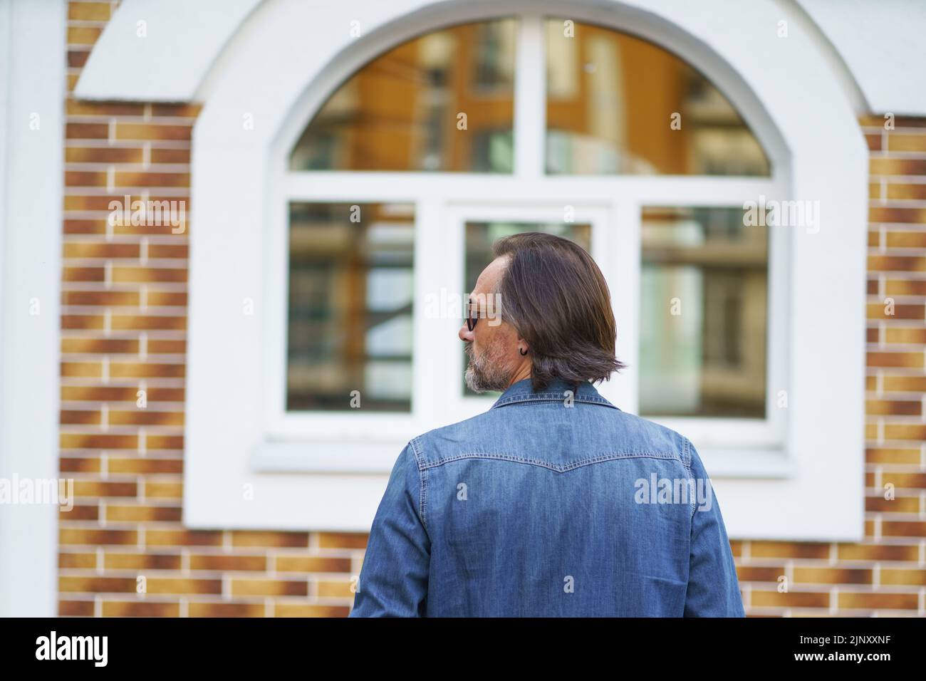 Close up rear view of a man standing alone in front old town building looking sideways while traveling in european cities during vacation time wearing denim jeans shirt. Travel concept.  Stock Photo