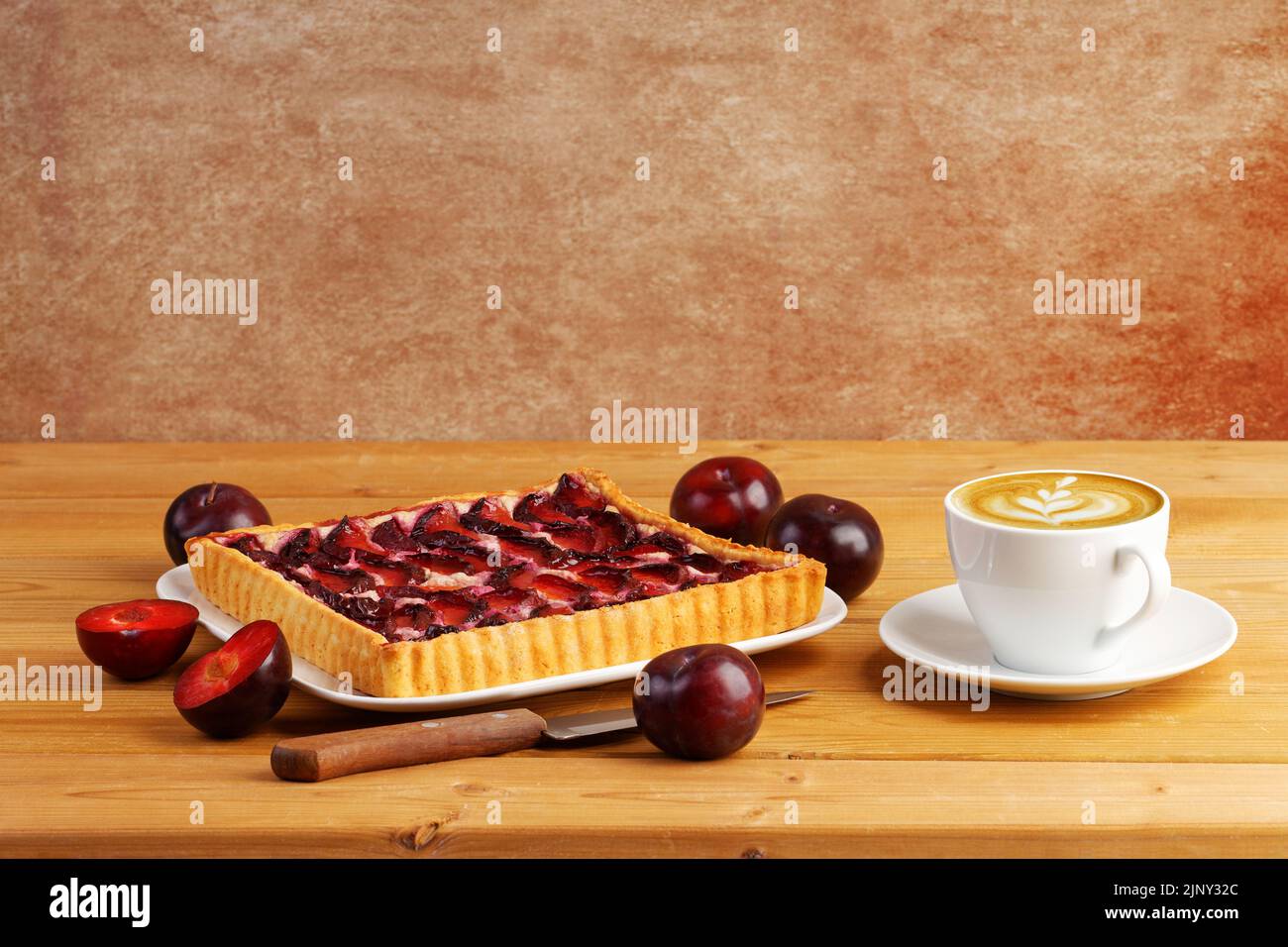 Homemade plum cake and cup of coffee cappuccino on wooden table. Copyspace. Stock Photo