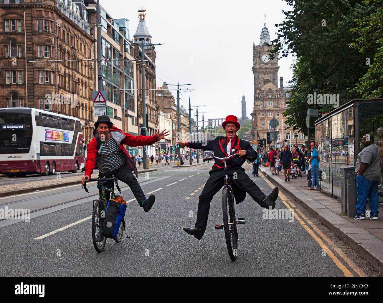 Princes Street, Edinburgh, Scotland, UK. EdFringe street performers, Todd Various on his adapted Penny Farthing bicycle and Mat Keys on his road bike have an unplanned fun race along Princes Street much to the amusement of passersby. Credit: Arch White/alamy live news. Stock Photo