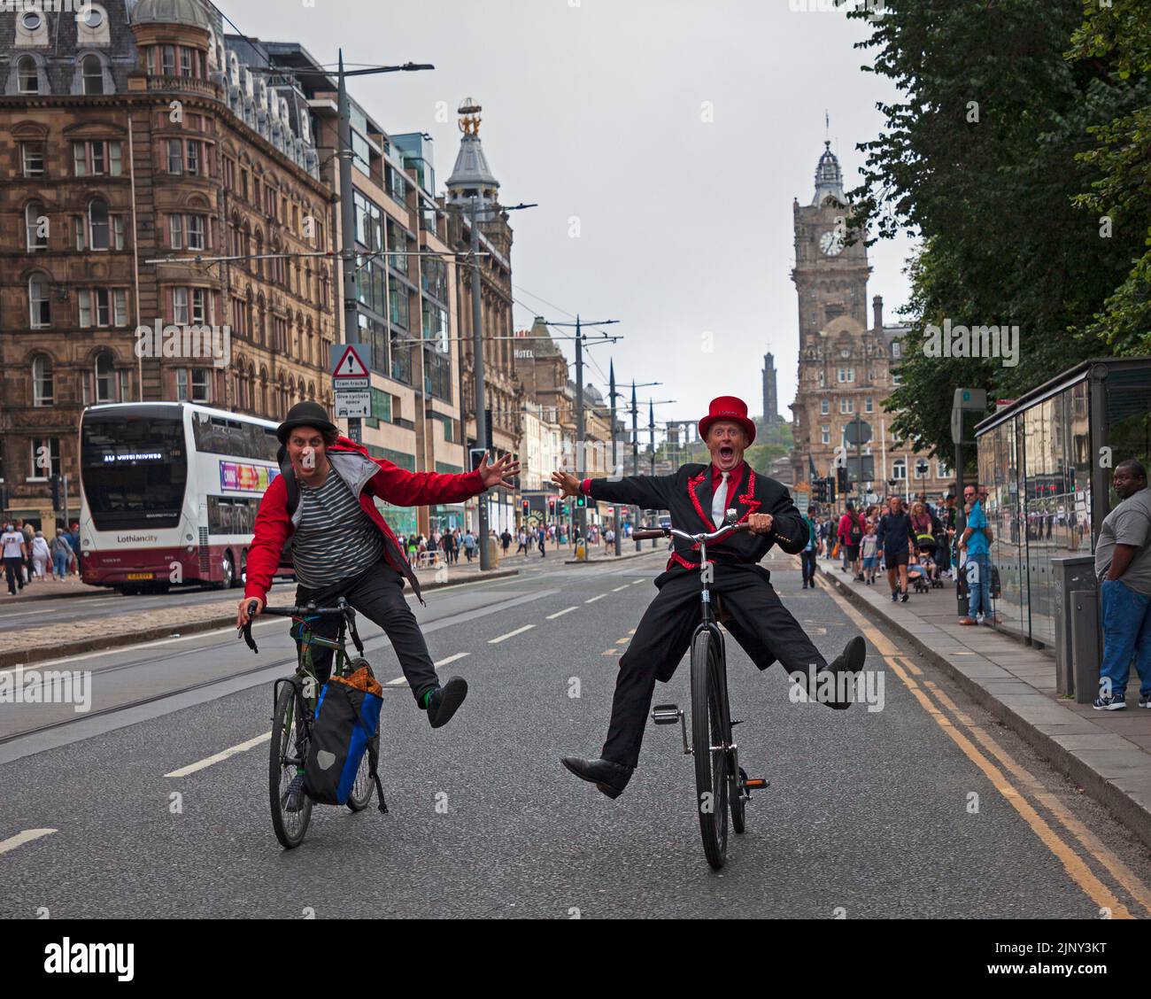 Princes Street, Edinburgh, Scotland, UK. EdFringe street performers, Todd Various on his adapted Penny Farthing bicycle and Mat Keys on his road bike have an unplanned fun race along Princes Street much to the amusement of passersby. Credit: Arch White/alamy live news. Stock Photo