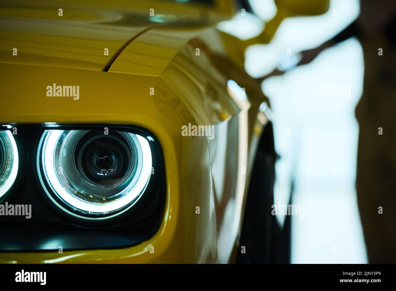 Headlight on the front part of luxurious electric car of yellow color standing on parking site, garage or workshop after repair Stock Photo