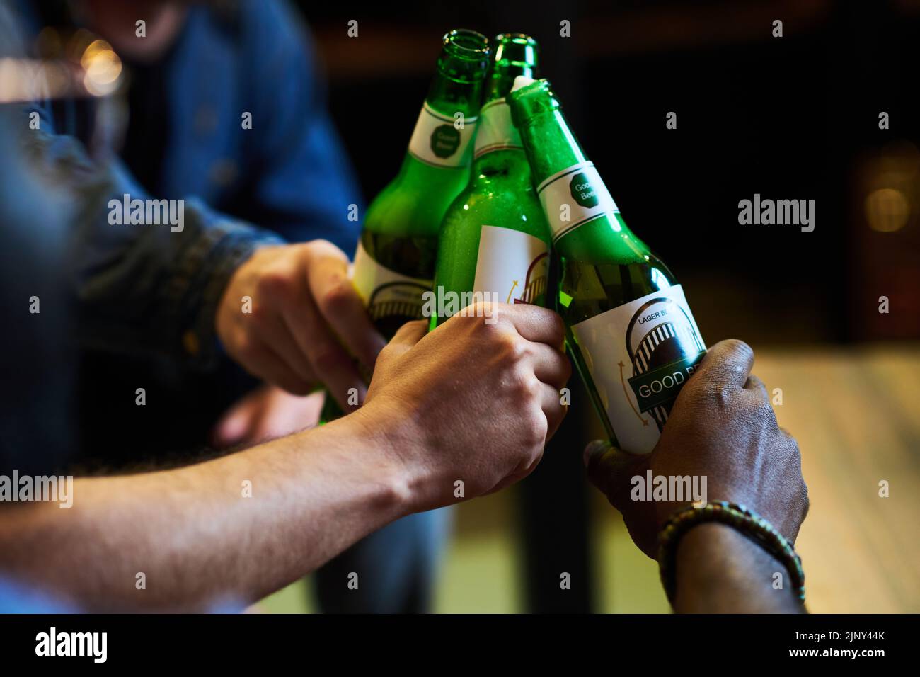 Hands of three young interracial men clinking with bottles of beer while enjoying gathering in garage or at home after work or on weekend Stock Photo