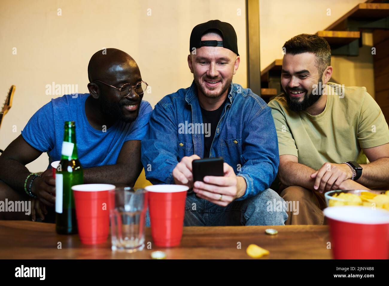 Young man with smartphone showing friends photos of his family or communicating in video chat while having nice time together Stock Photo