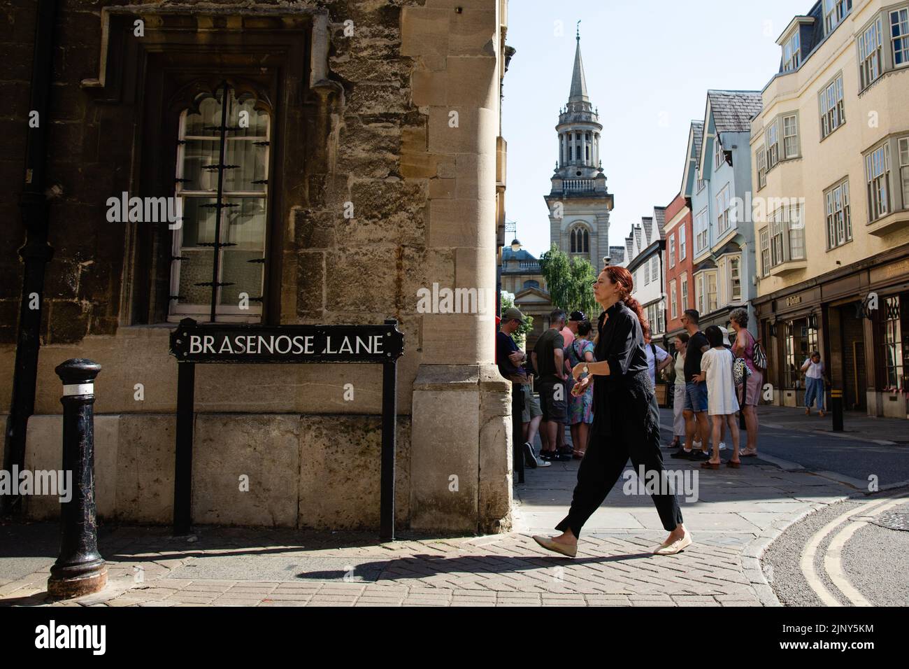 Oxford, UK. 12th August, 2022. A woman passes in front of a group of tourists in Turl Street on a hot summer's day. Hot and dry conditions continue ac Stock Photo