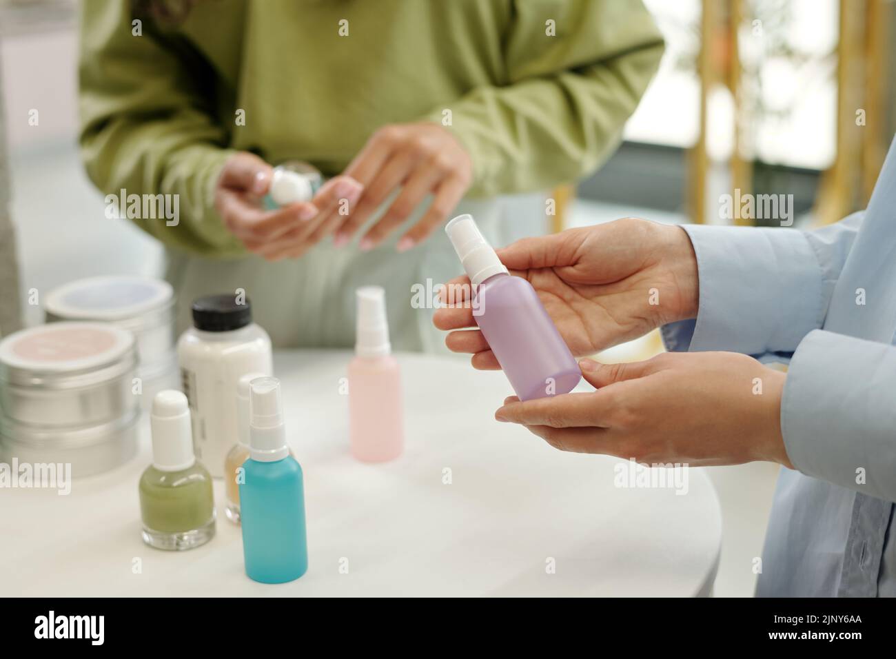 Hands of young female shopper holding plastic bottle with sprayer containing liquid beautycare product while standing by display Stock Photo