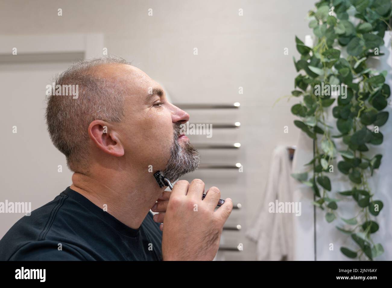 Middle-aged handsome man using razor in bathroom Stock Photo
