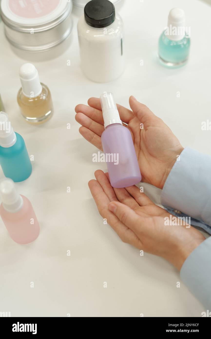 Hands of young female shopper holding plastic bottle with cosmetic product over idsplay with assortment of nailcare goods Stock Photo