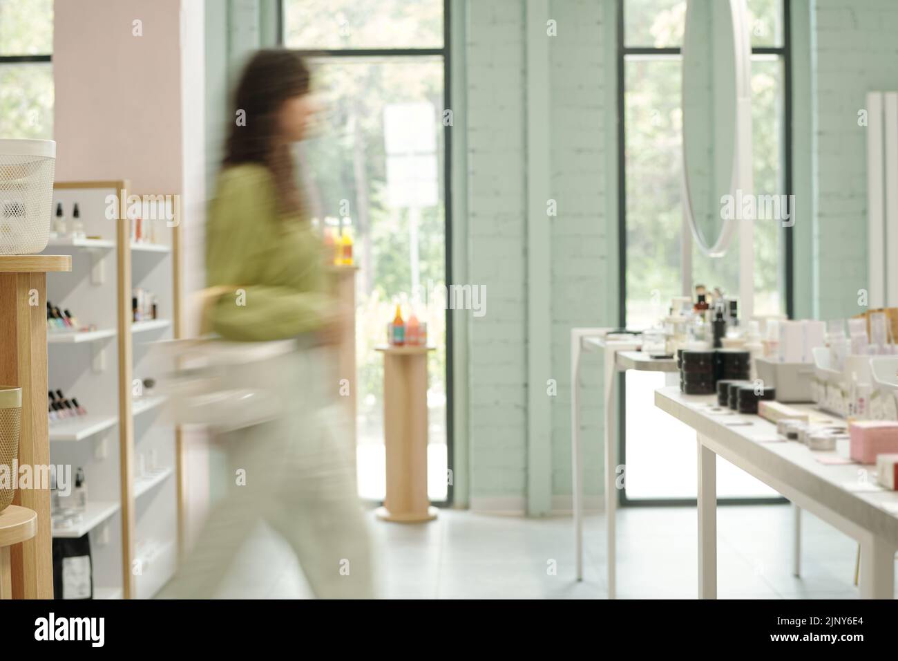 Interior of spacious beautycare supermarket with blurry motion of young female consumer walking along displays with cosmetic products Stock Photo