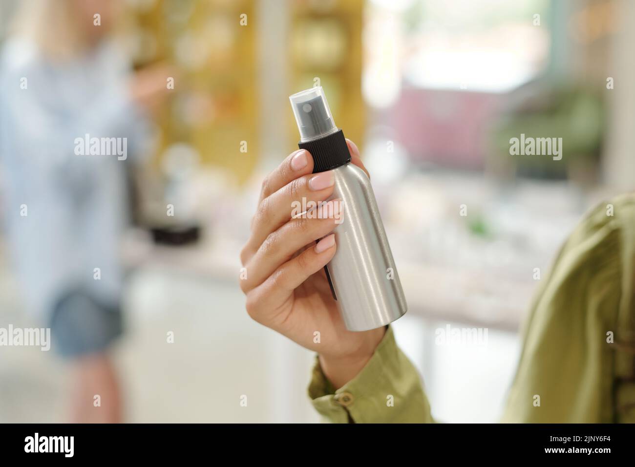 Hand of young woman holding small metallic bottle with sprayer containing liquid haircare product such as spray wax or dry oil Stock Photo