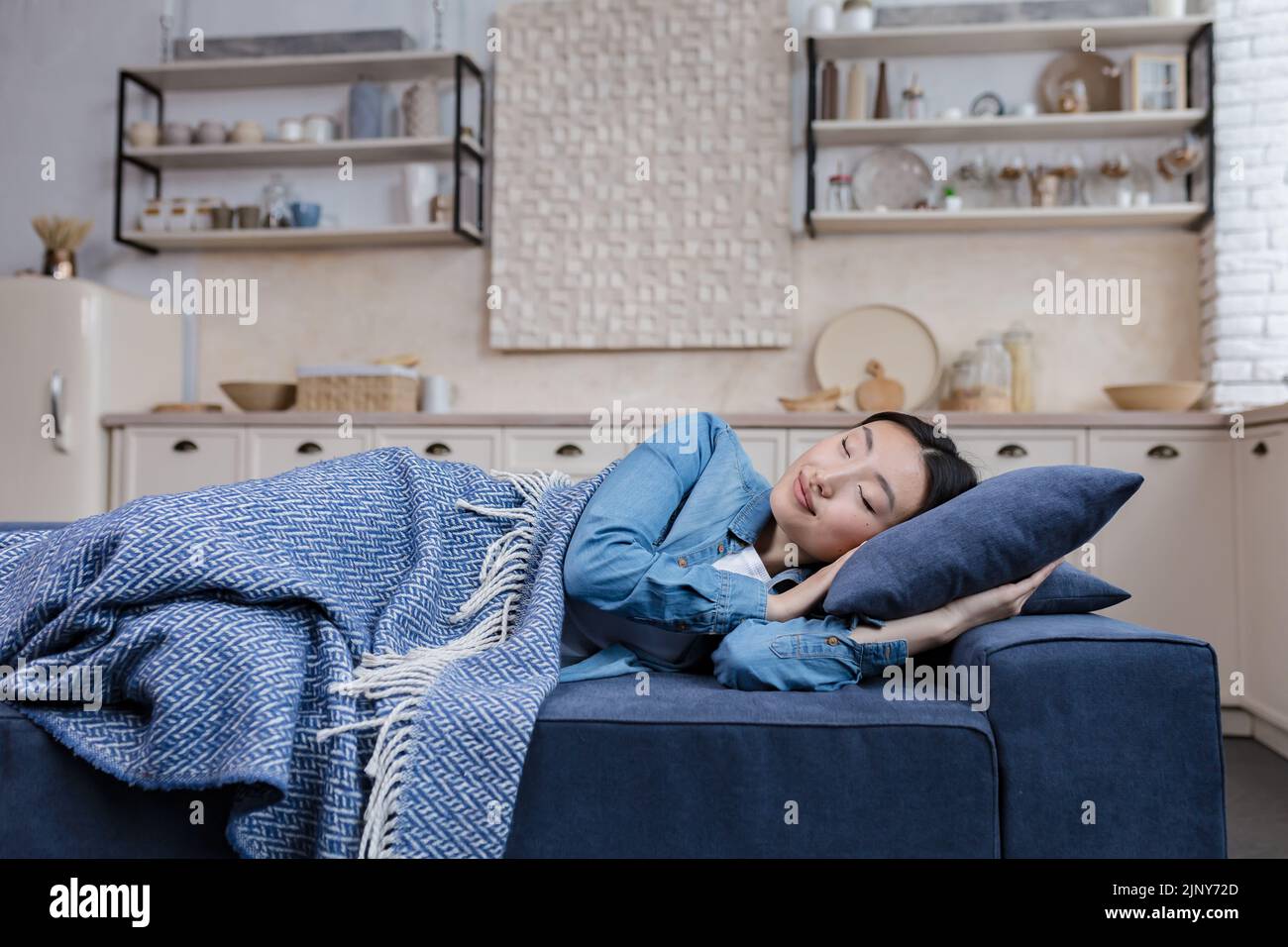 Young beautiful Asian woman resting and sleeping at home lying on sofa under blanket in living room, day nap Stock Photo