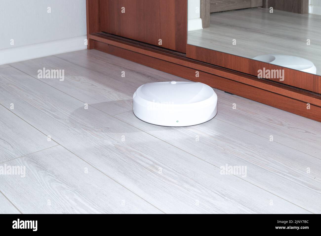 A small robot vacuum cleaner works on the floor, vacuuming the laminate. House cleaning, smart gadgets. Stock Photo