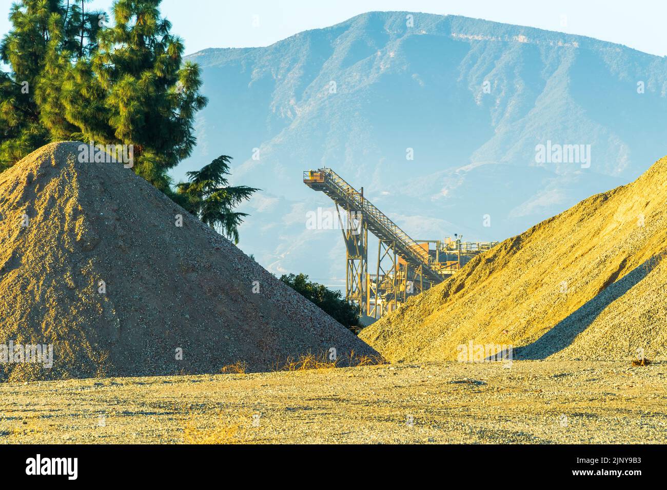 Stone quarry crusher and belt conveyor as seen between piles of stone aggregate. Stock Photo