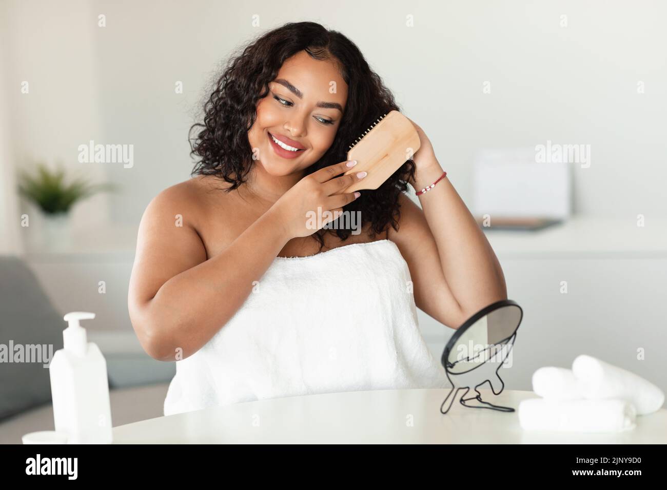 Happy african american oversize woman brushing her curly hair with comb ...