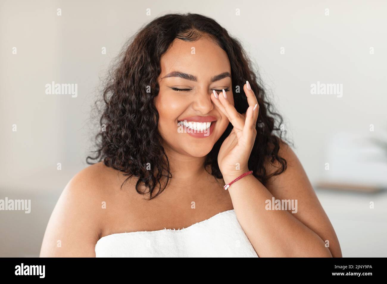 Natural essential beauty. Joyful black plus size lady with closed eyes touching her soft flawless skin, laughing Stock Photo