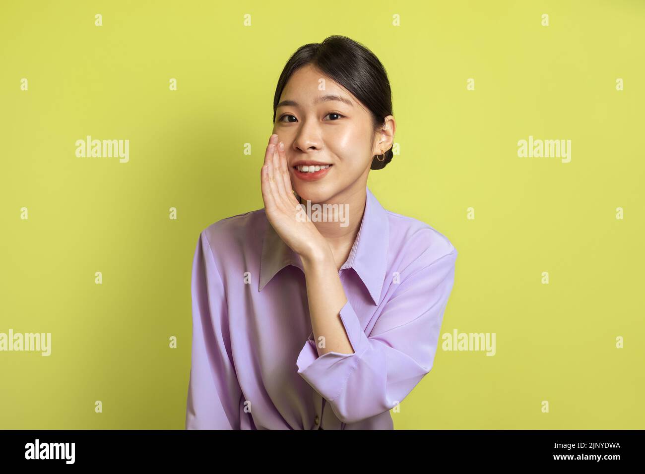 Smiling Japanese Woman Whispering Holding Hand Near Mouth, Yellow Background Stock Photo