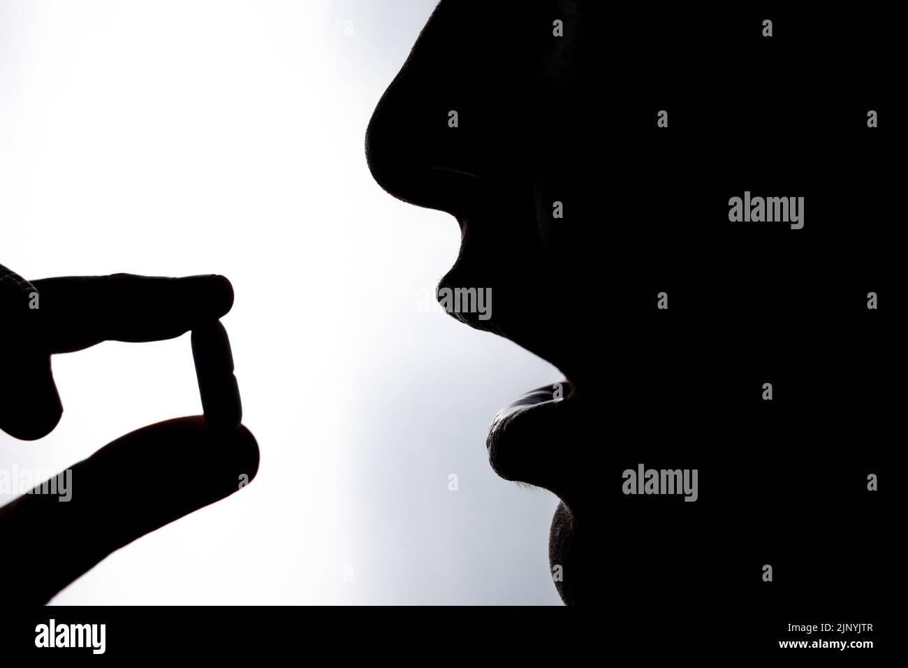 Taking pill. Silhouette of a unrecognizable woman taking a pill or drug. Healthcare or medicine or wellness or taking vitamins or recovering from illn Stock Photo