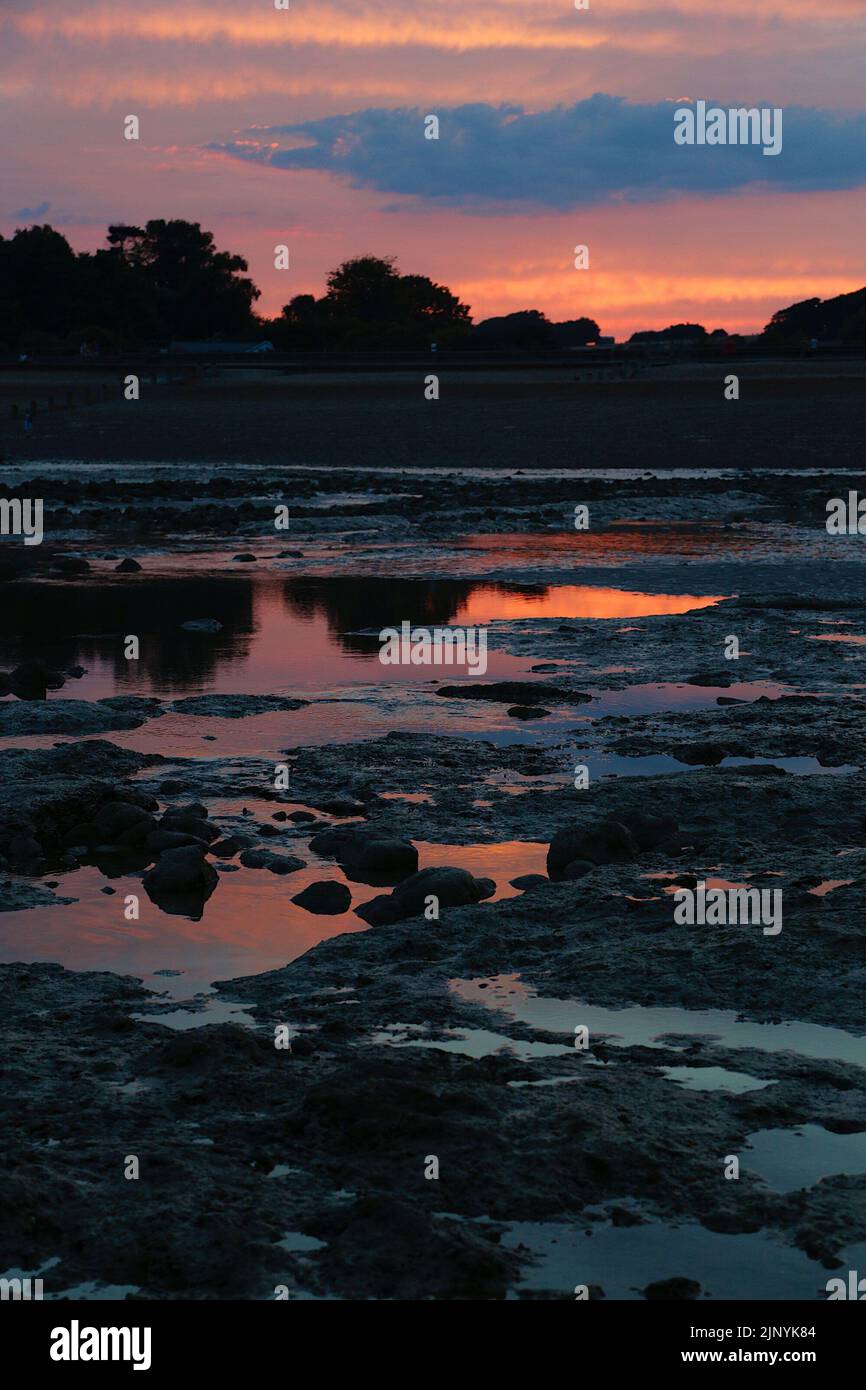 Pett Level, East Sussex, UK. 14 Aug, 2022. UK Weather: The sun goes down in a red glow illuminating a submerged ancient forest only visible at low tide. Photo Credit: Paul Lawrenson/Alamy Live News Stock Photo