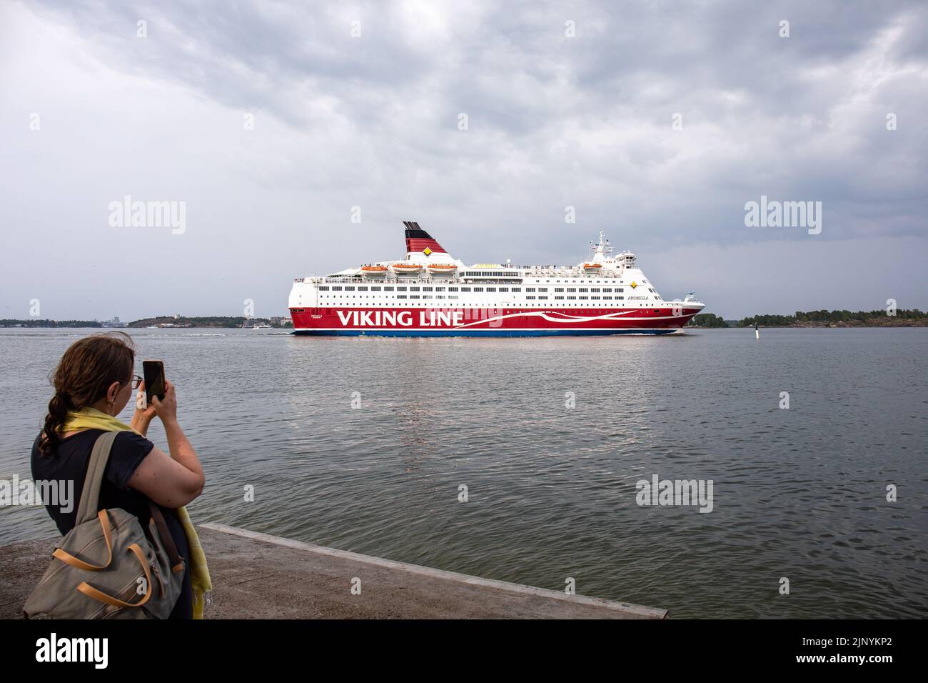 Woman taking picture of cruise ship M/S Amorella of Viking Line shipping company passing Lonna Island in Helsinki, Finland Stock Photo