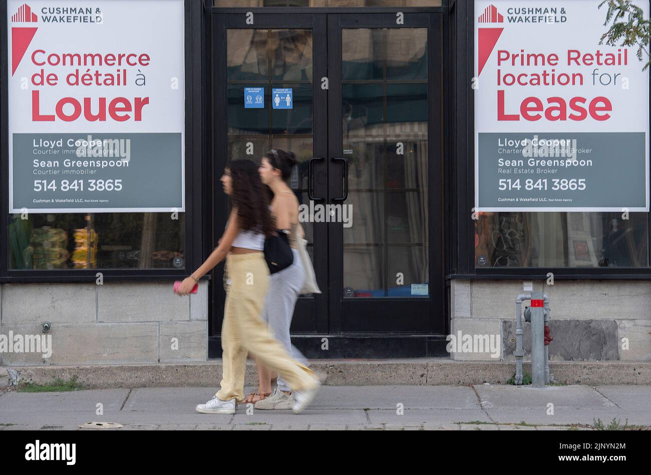 People walk by bilingual signs for a commercial space for lease in the