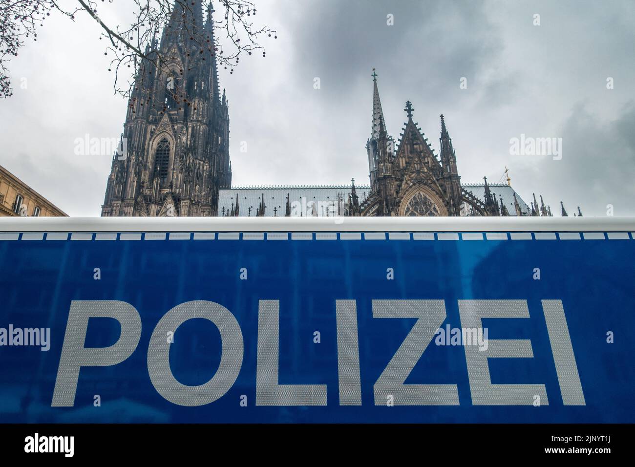 View past a German police car sign at the Cologne cathedral (Kölner Dom) under ominous dark clouds in Cologne, Germany. Stock Photo