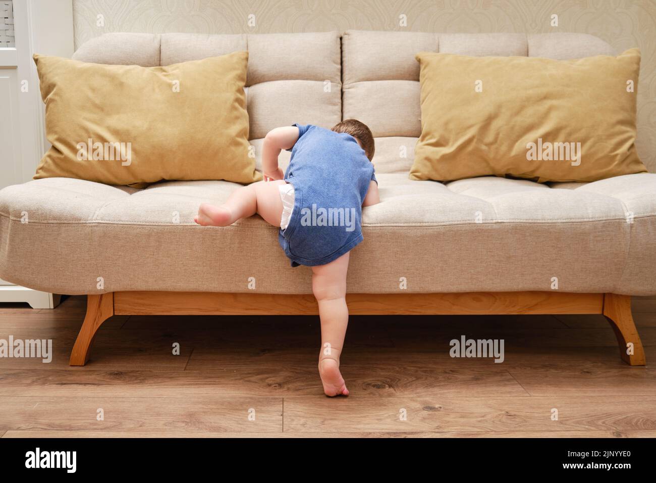 Toddler baby climbs on the sofa. Child boy learning to get off the bed